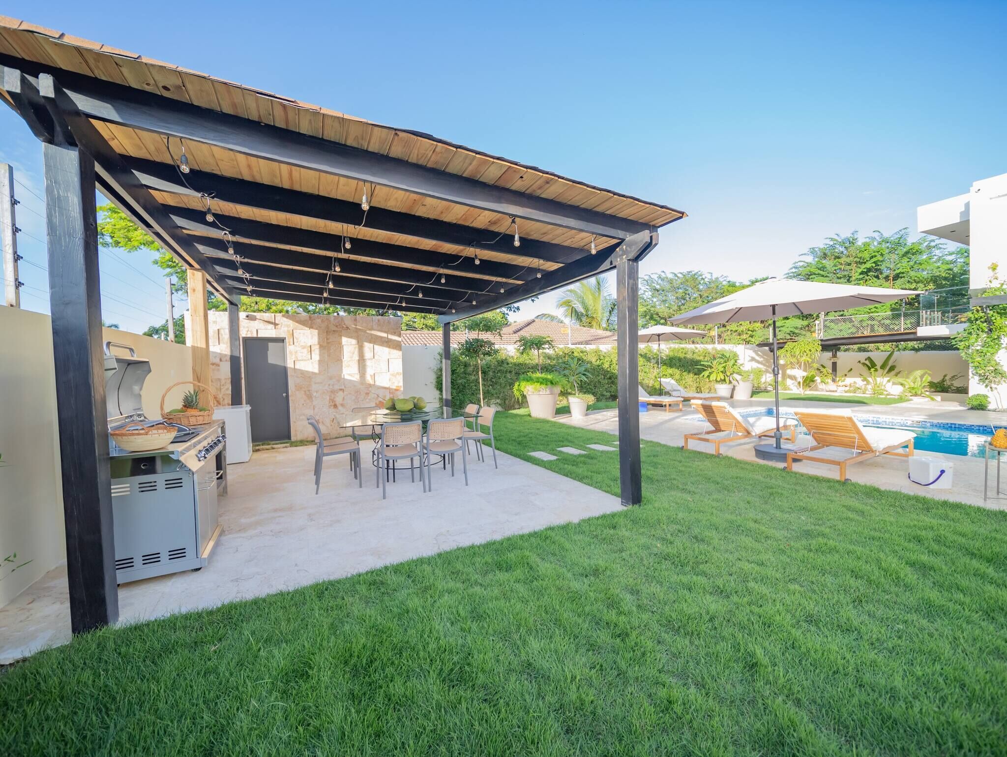 Eine überdachte Terrasse im Freien mit Grill, Sitzgelegenheiten und Poolbereich.