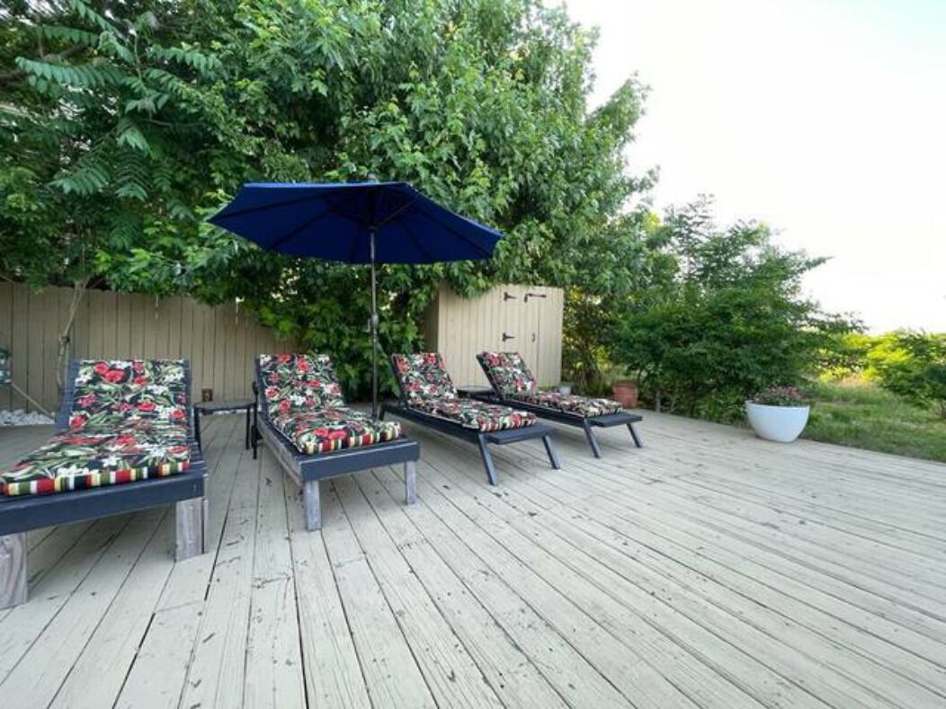 A wooden deck with lounge chairs and a blue umbrella.
