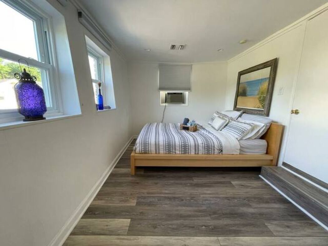 A bedroom with a wooden bed, a window with a decorative lantern, a painting on the wall, and a ceiling light.