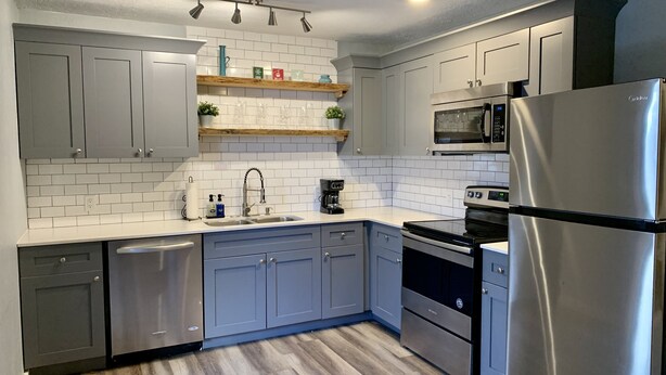 A modern kitchen with grey cabinets, white subway tiles, stainless steel appliances, and wooden flooring. - Kennedy’s Camelot, a walkable family condo in beautiful Angel Fire! (Angel Fire)