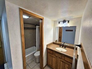 Un baño con tocador de madera, un lavamanos blanco, un espejo y una zona de ducha.