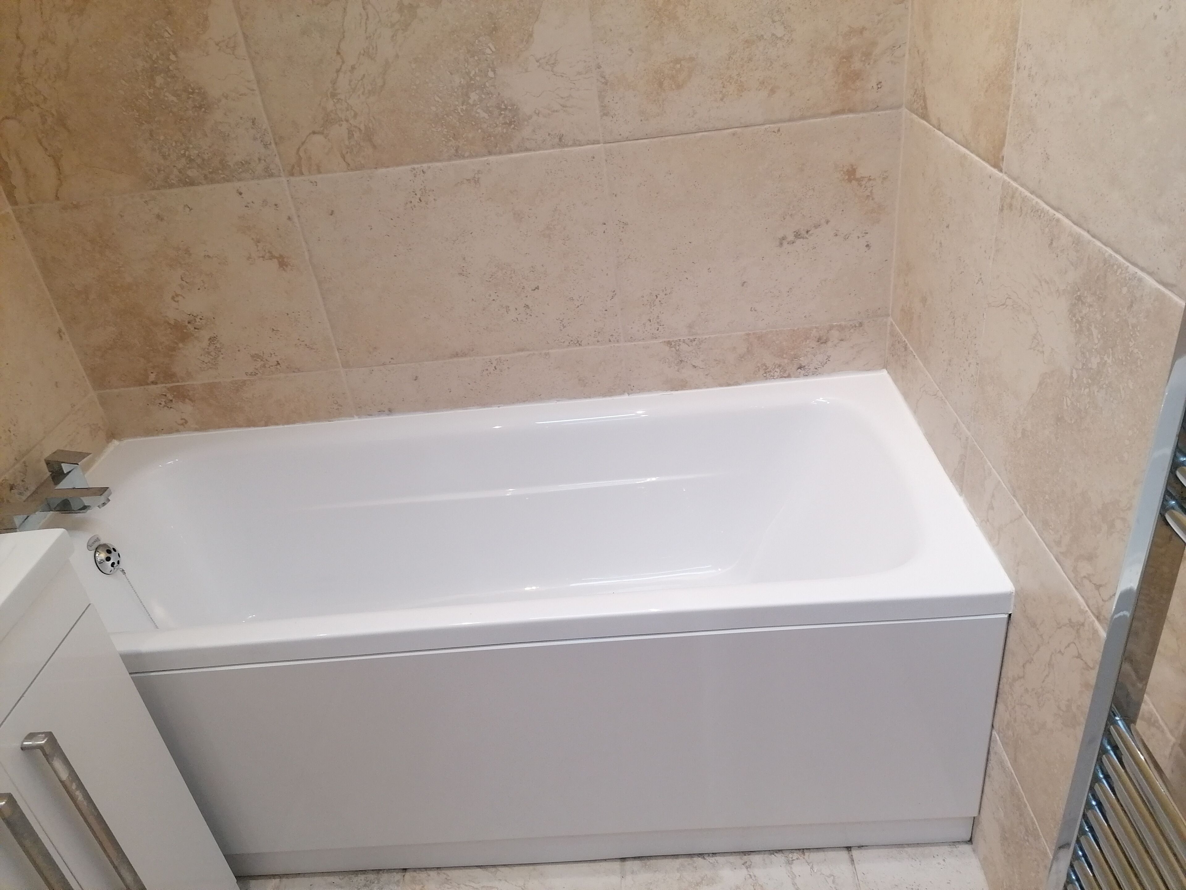 Eine weiße Standardbadewanne in einem Badezimmer mit beige gefliesten Wänden.