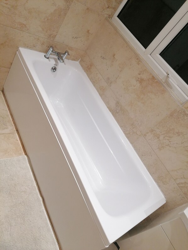 A white bathtub in a bathroom with beige tiled flooring and a white door in the background. - 92 Seaford Street (Stoke-on-Trent)