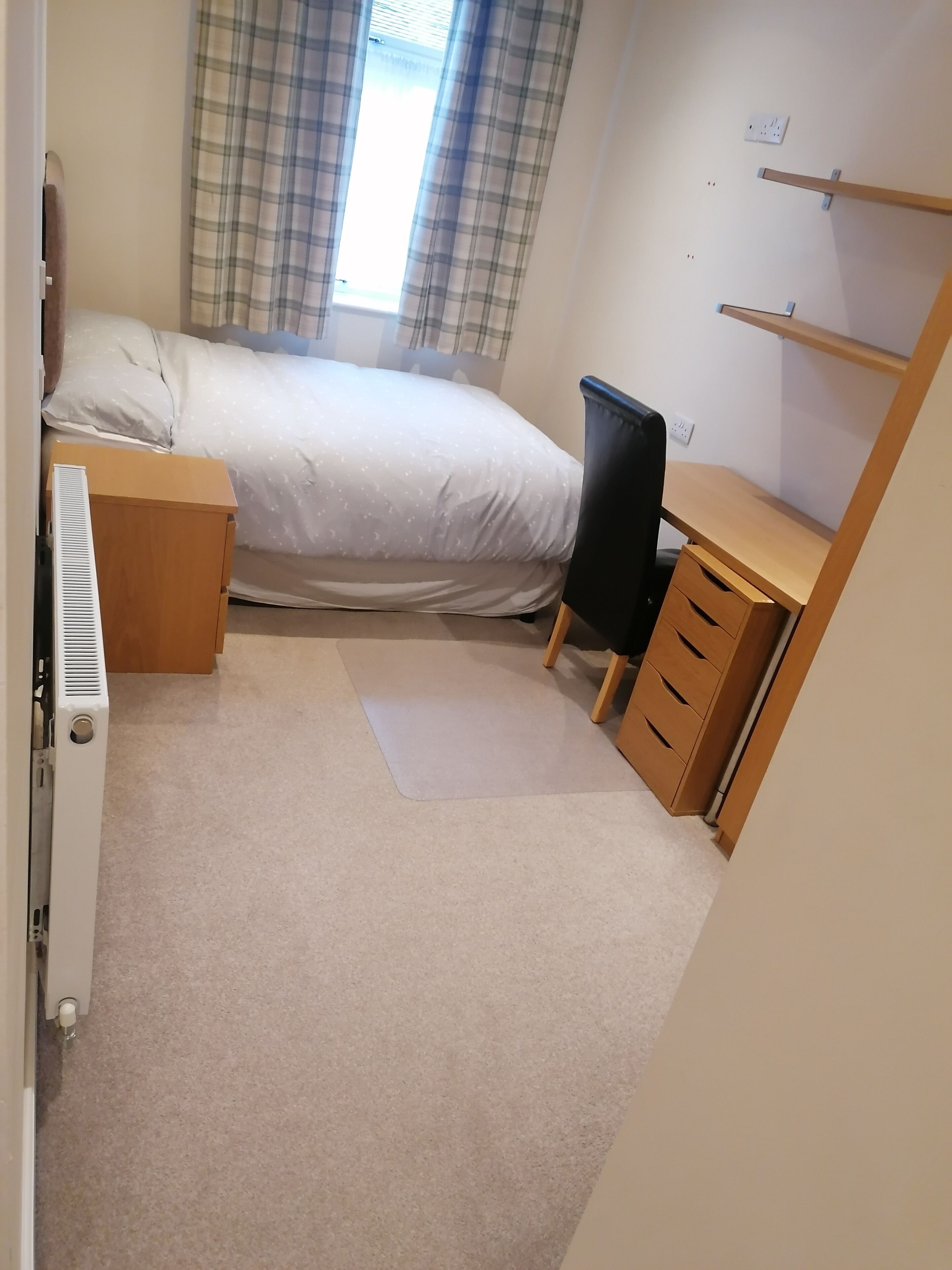 Ein Schlafzimmer mit Bett, Schreibtisch, Stuhl und Heizkörper.