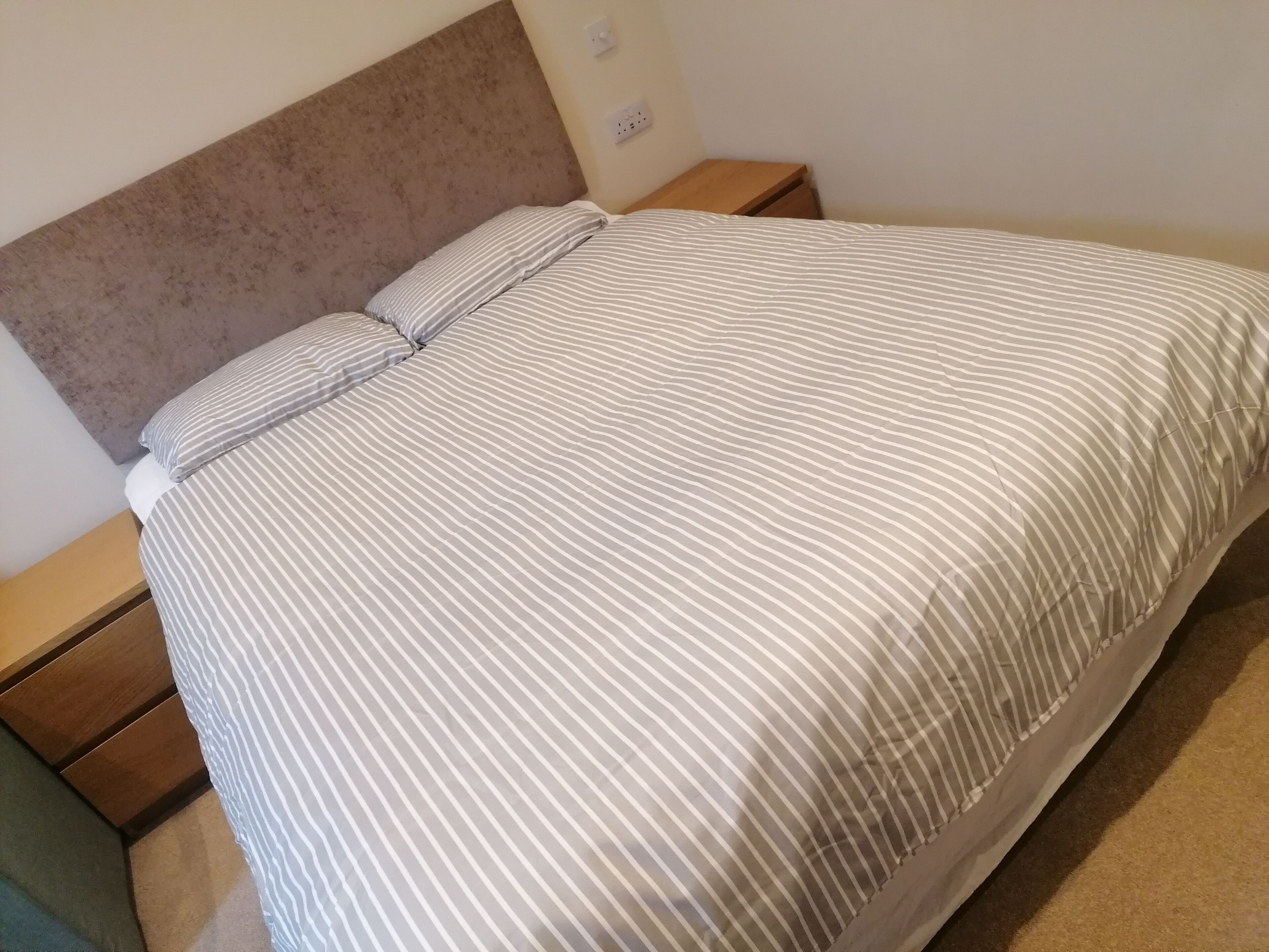 A bed with a striped bedspread and pillows, a wooden headboard, and a nightstand with a lamp.