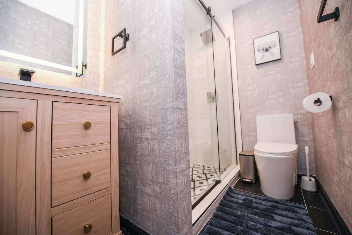 A bathroom with a wooden vanity, a glass shower enclosure, a toilet, and a towel rack.
