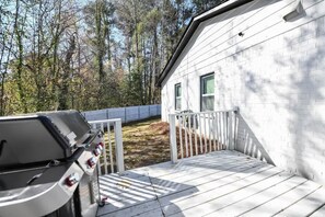 A house with a deck, a barbecue grill, and a white fence.