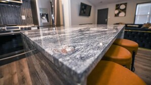 Une cuisine dotée d’un plan de travail en granit, d’un four moderne et d’un coin repas avec des tabourets orange.