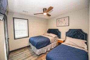 A bedroom with two beds, a ceiling fan, a window with blinds, and a framed picture on the wall.
