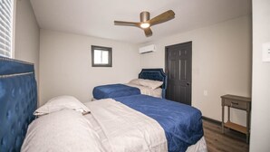Une chambre avec deux lits, un ventilateur de plafond, une fenêtre, un climatiseur et une porte.