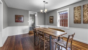 Comedor con mesa y sillas de madera, un candelabro y cuadros en las paredes.