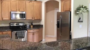 A kitchen with wooden cabinets, a stainless steel refrigerator, a microwave, an oven, and granite countertops. - Amazing Centrally Located Home in Peaceful Area (Jacksonville)