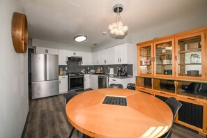A modern kitchen with a round wooden table, stainless steel appliances, and a glass-fronted cabinet.
