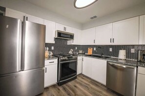 A modern kitchen with stainless steel appliances, white cabinets, and a herringbone-patterned backsplash.