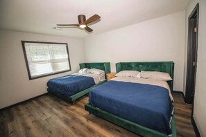A bedroom with two beds, a ceiling fan, a window with blinds, and a wooden floor.