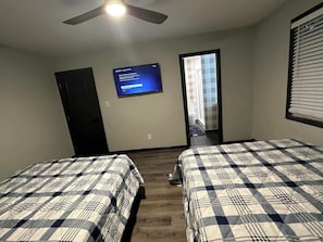 A bedroom with two beds, a ceiling fan, a TV, and a door leading to a bathroom.