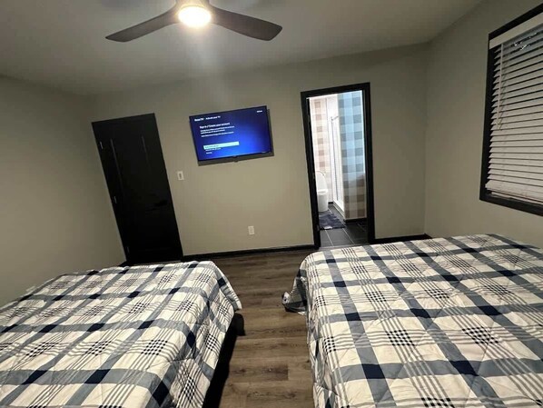 Une chambre avec deux lits, un ventilateur de plafond, une télévision et une porte donnant sur une salle de bain.