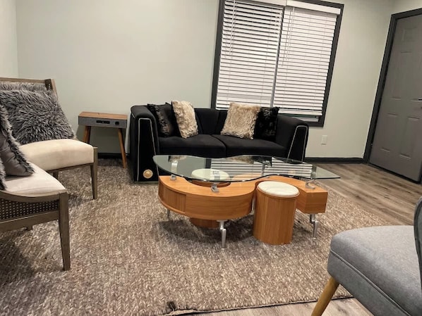 A modern living room with a black sofa, a glass coffee table, and a wooden side table.