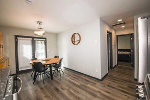 A modern kitchen with a built-in oven, a dining area with a wooden table and chairs, and a hallway leading to a bedroom.