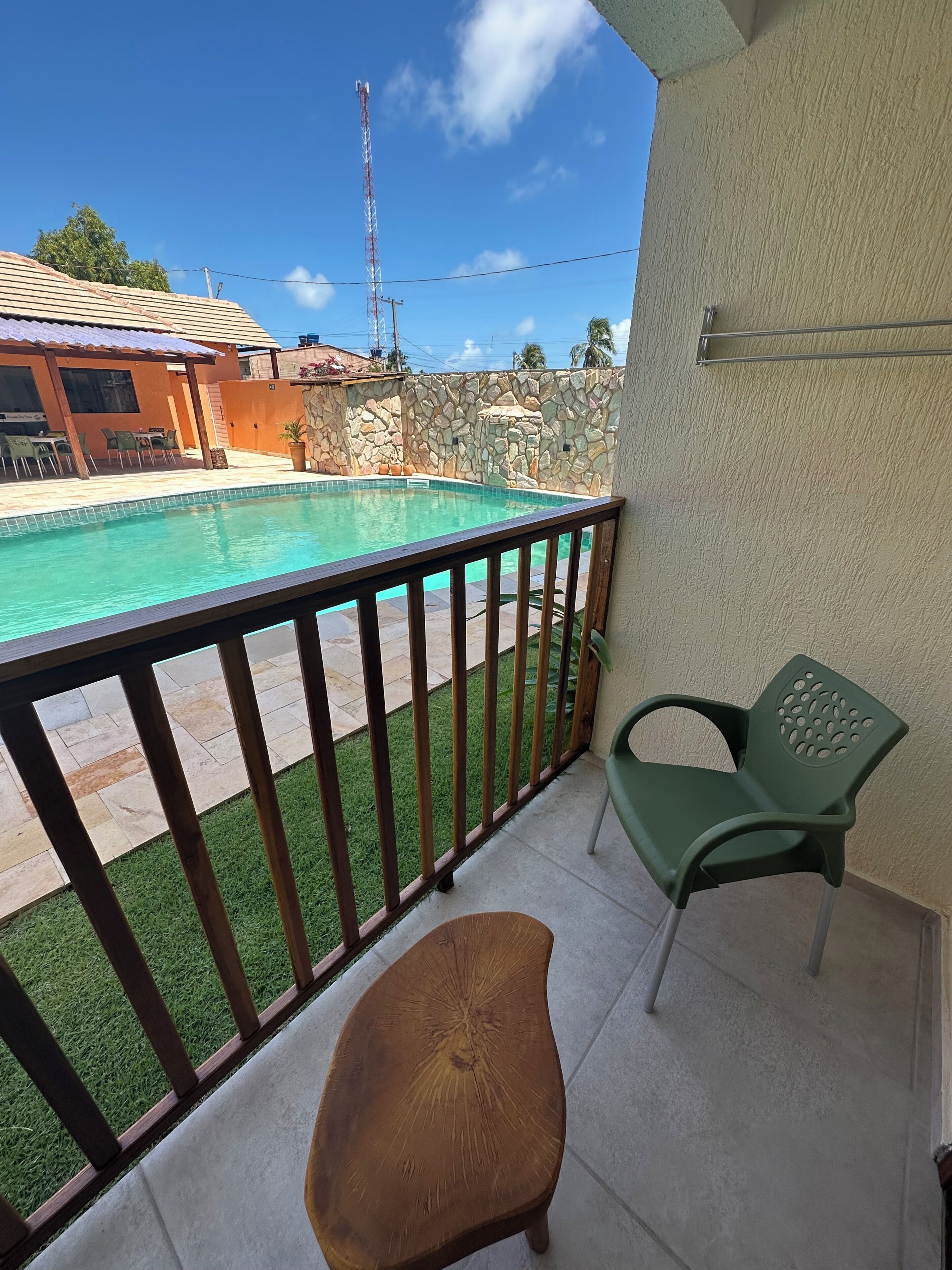 A balcony with a pool, a stone wall, and a view of a building with a tiled roof.