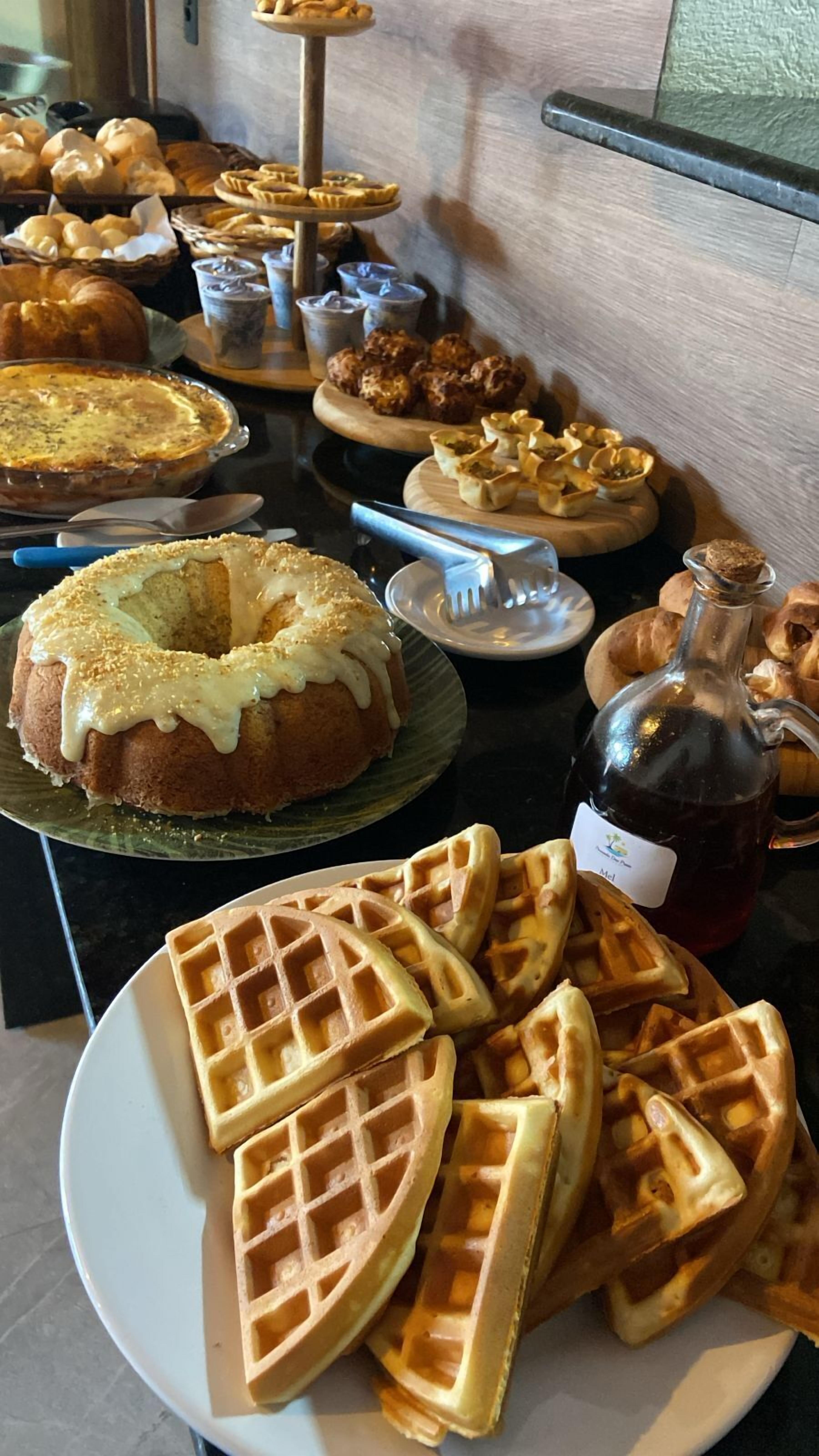 A buffet table with various baked goods including a bundt cake, waffles, muffins, and pastries.