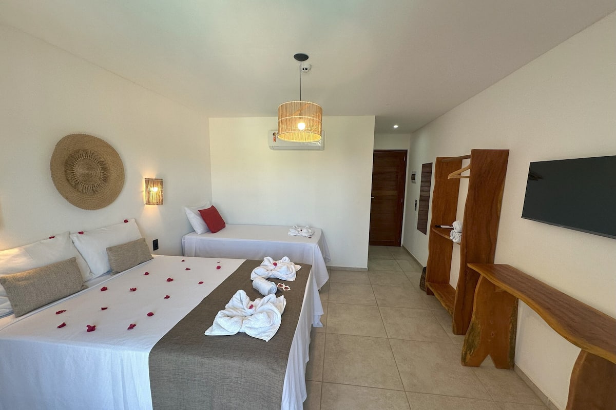 A hotel room with two beds, a TV, a wooden bench, and a wall-mounted TV.