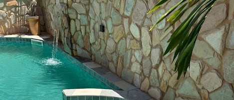 Piscina con pared de piedra y una pequeña cascada.