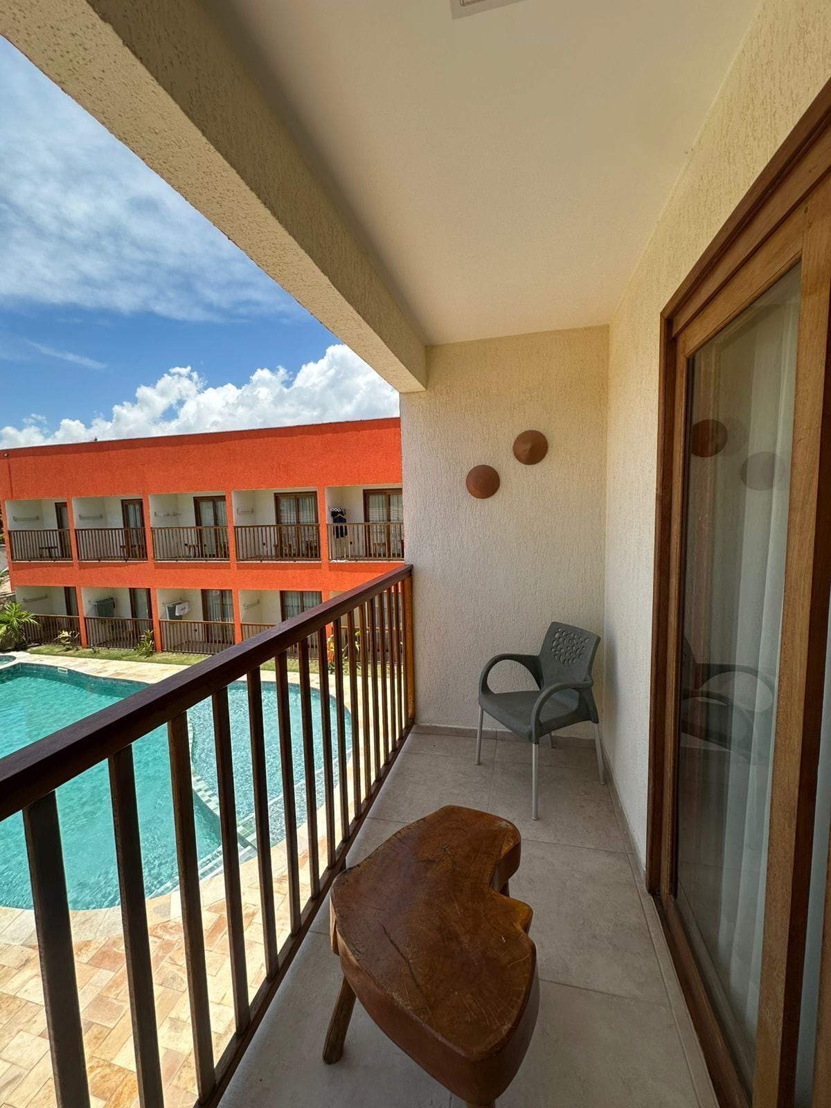 Un balcón con vista a la piscina, una silla y un banco de madera.