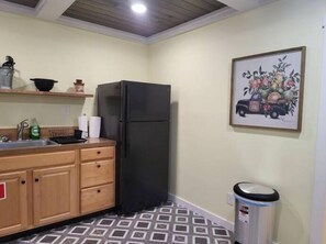 A compact kitchen with wooden cabinets, a black refrigerator, a sink, and a trash bin.