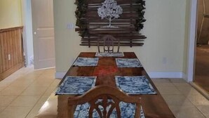 A dining area with a wooden table and chairs, a decorative wall piece above the table, and a tiled floor. - Bear Mountain Farm 2.0 (Monroe)