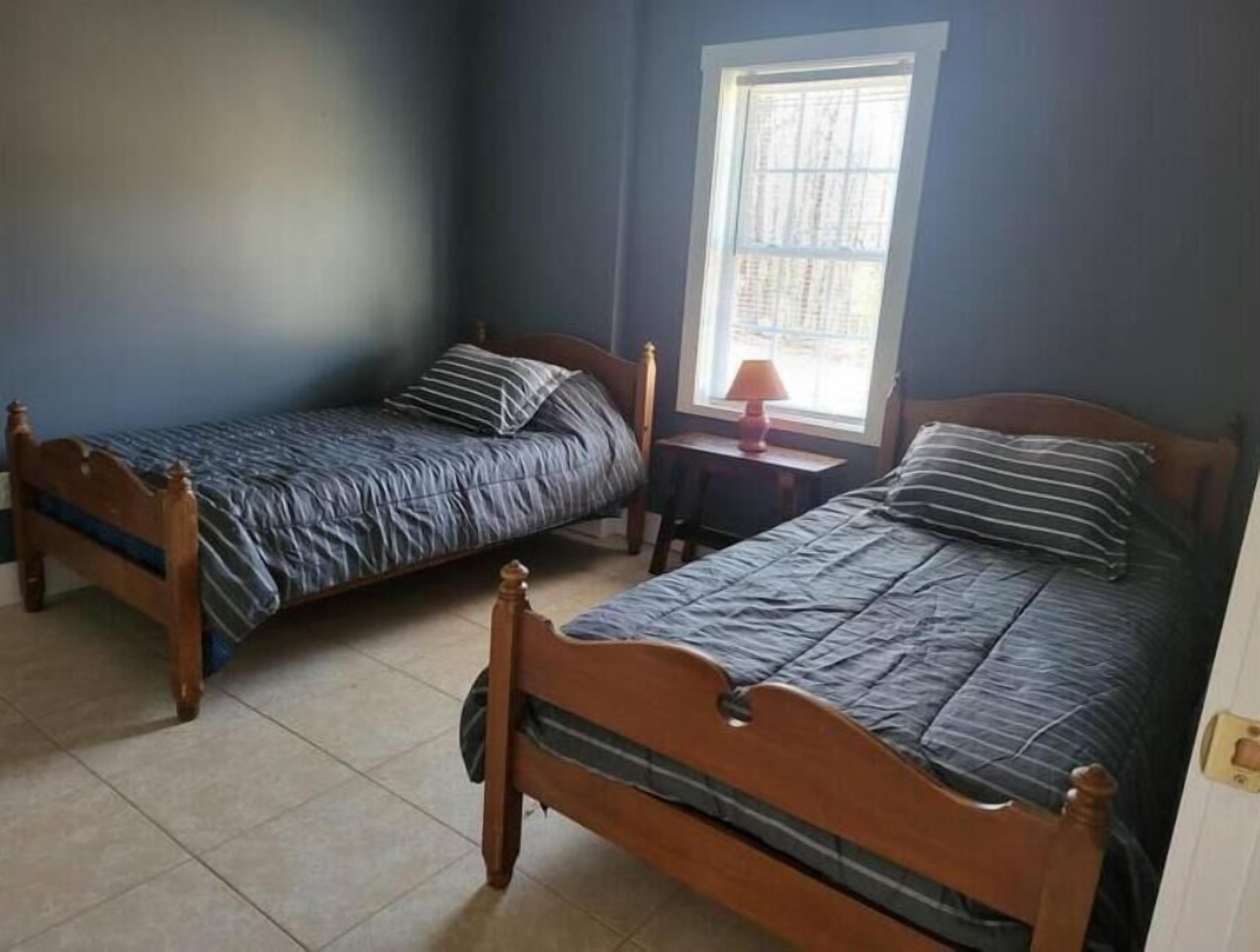 Two wooden beds with dark bedding in a room with a window.