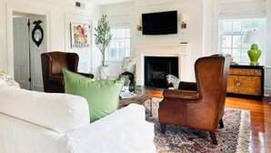 Ein Wohnzimmer mit einem weißen Sofa, einem braunen Sessel, einem Kamin und einem an der Wand befestigten Fernseher.