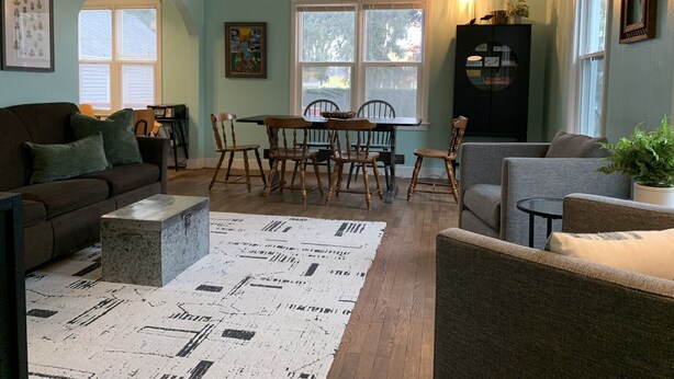 Ein gemütliches Wohnzimmer mit einer Couch, Sesseln, einem Esstisch und einem Teppich.