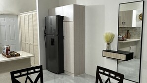 Een moderne keuken met een inbouwkoelkast, een eethoek met een glazen tafel en stoelen, en een grote spiegel aan de muur.