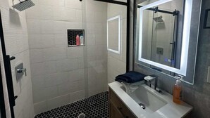 Ein modernes Badezimmer mit Dusche, Waschbecken, Spiegel und einer kleinen Ablage für Toilettenartikel.