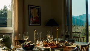 Een eettafel gedekt met borden, glazen en kaarsen, met een prachtig uitzicht door grote ramen.
