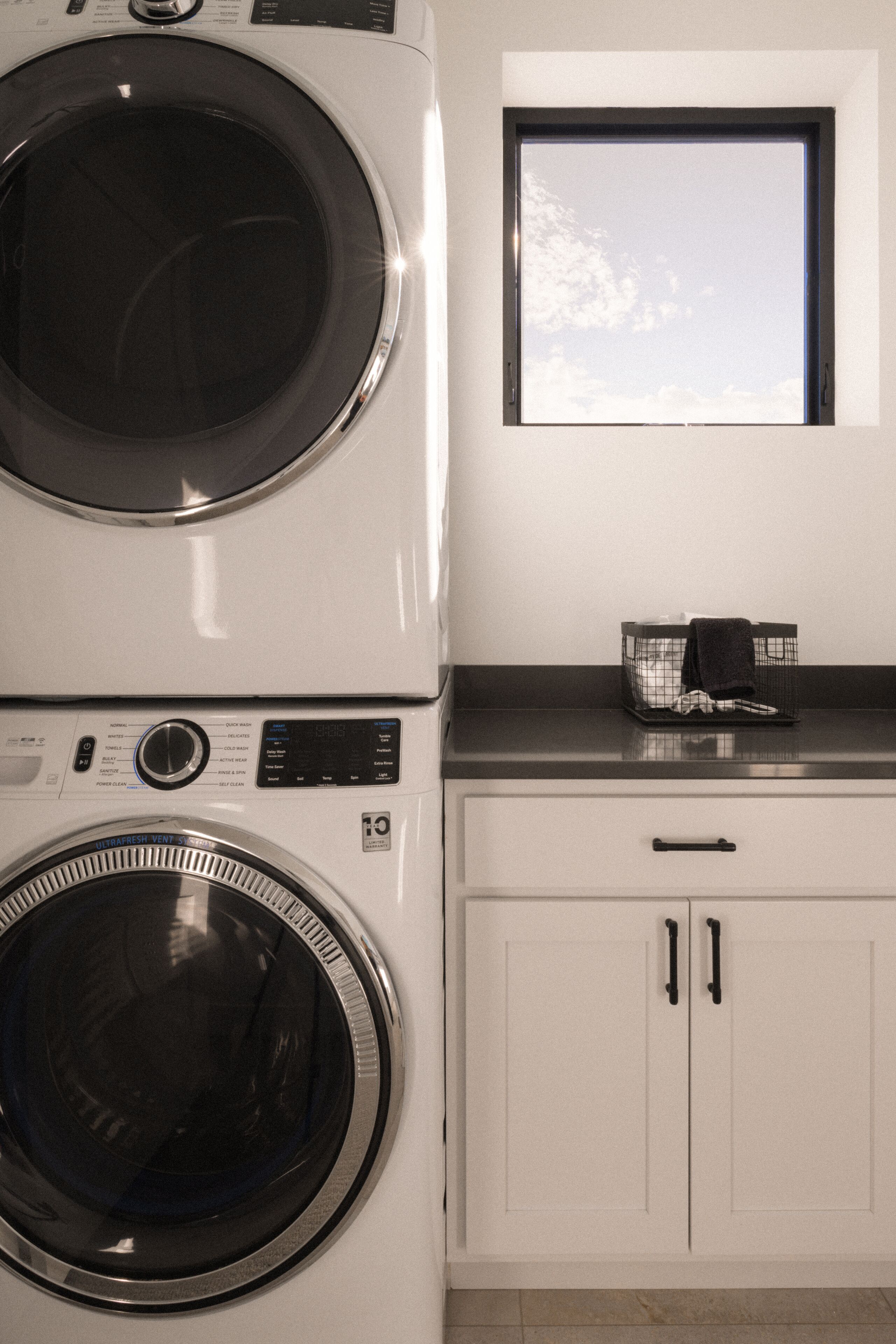 A laundry area with stacked washers and dryers, a window, and a countertop with a basket.