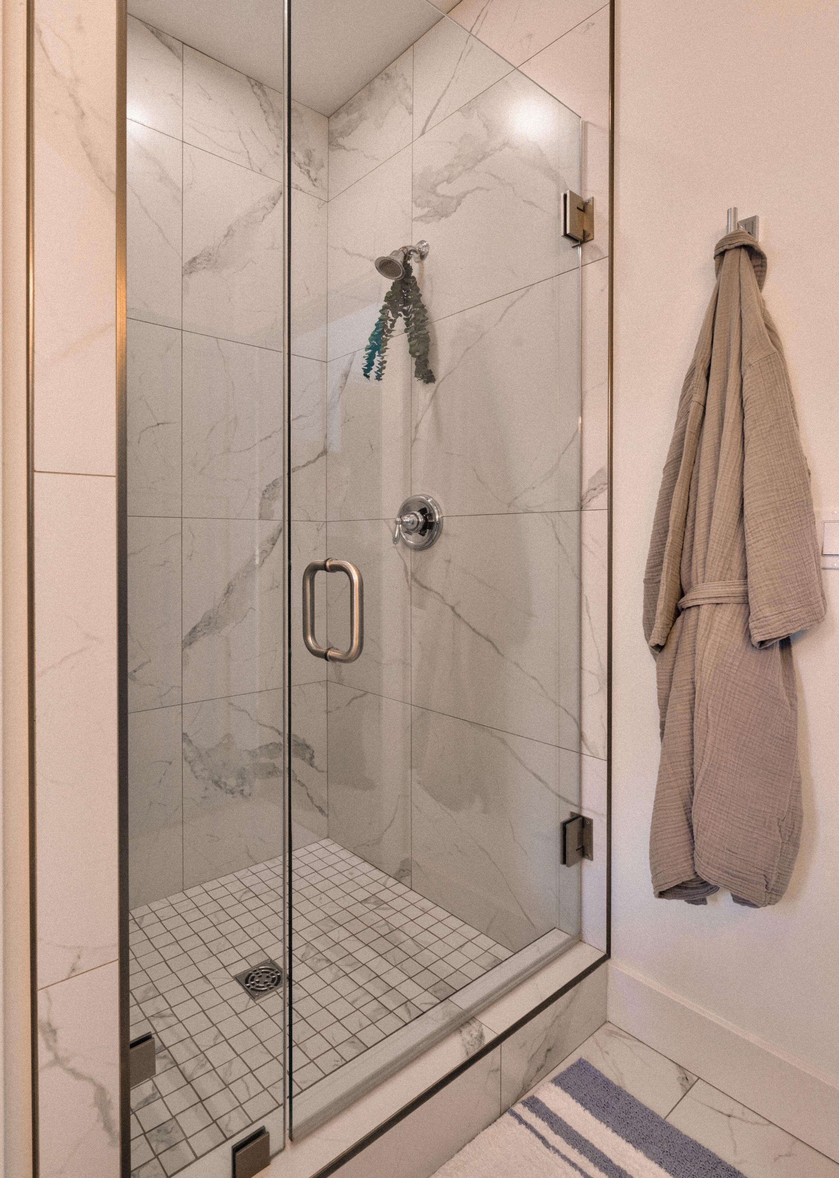 A glass-enclosed shower with a marble floor, a towel rack with a towel, and a shower control panel.