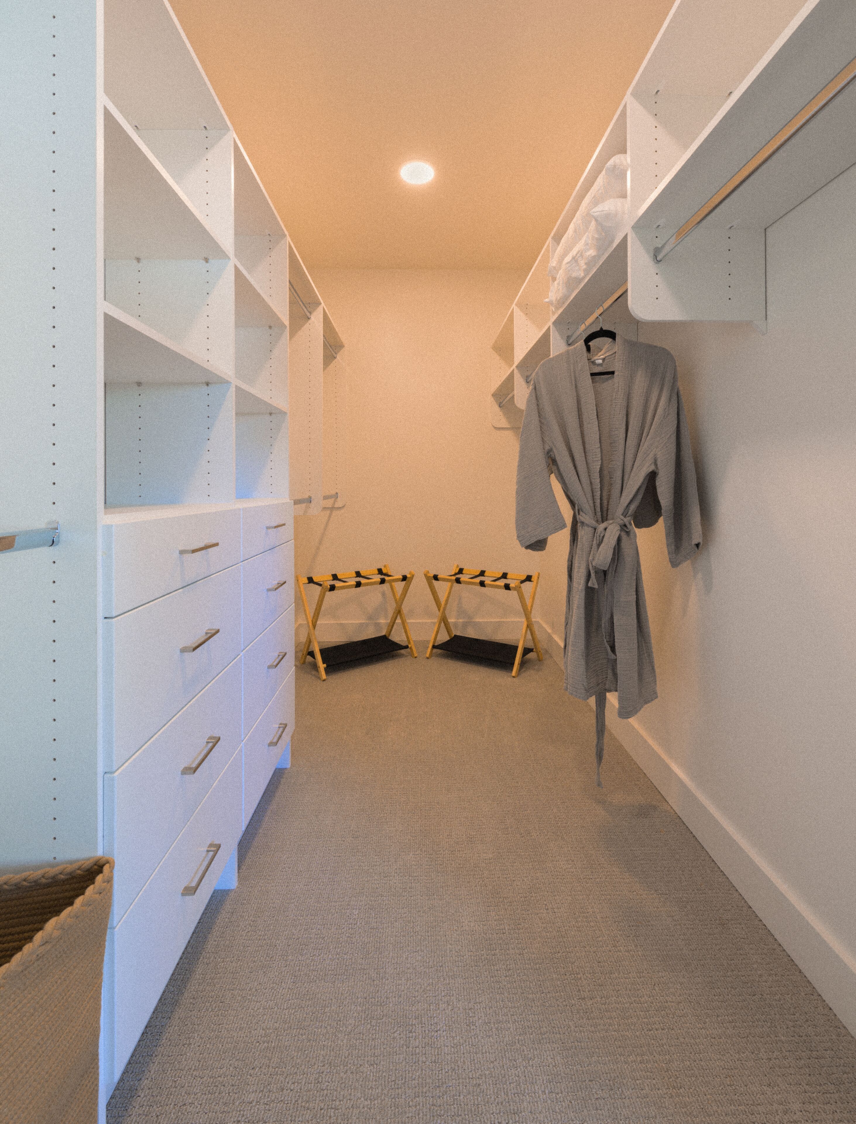 A walk-in closet with white shelving units, a hanging robe, and a shoe rack.