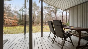A covered patio with a wooden table and chairs, overlooking a yard with trees and a grassy area.