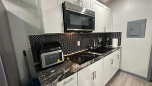 A kitchen with white cabinets, a black microwave, a gas stove, and a herringbone-patterned backsplash.