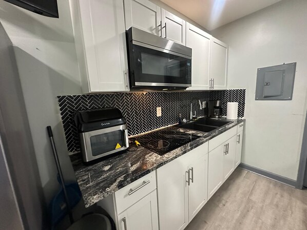 A kitchen with white cabinets, a black microwave, a gas stove, and a herringbone-patterned backsplash.