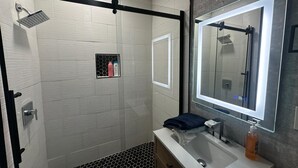 A modern bathroom with a glass shower enclosure, a large mirror, and a white sink.