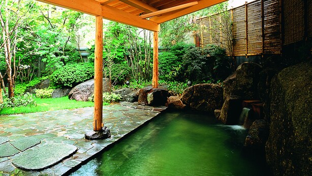 Un sendero de piedra que conduce a una fuente de agua en un jardín con bambú y follaje.