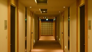 Un pasillo de hotel con puertas a ambos lados, un muro de azulejos al final e iluminación empotrada.