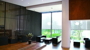 Un interior moderno con piso de madera, muebles negros y amplios ventanales que ofrecen vista a la vegetación.