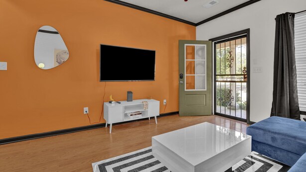 A modern living room with a large flat-screen TV, a white console table, a blue sofa, and a large mirror on the orange wall. - Fun & Funky #2 centrally located in Memphis! (Memphis)