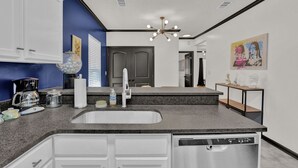 A modern kitchen with a granite countertop, white cabinets, a built-in dishwasher, and a unique chandelier. - Fun & Funky #2 centrally located in Memphis! (Memphis)