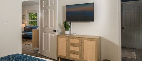 A bedroom with a bed, a television mounted on the wall, a wooden cabinet, and a door leading to another room.