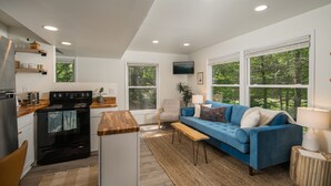 A modern kitchen with a built-in stove, wooden countertops, and a large window. There is a blue sofa with a wooden coffee table and a lamp. - Riverview Retreat at The Wanderer  (Boone)